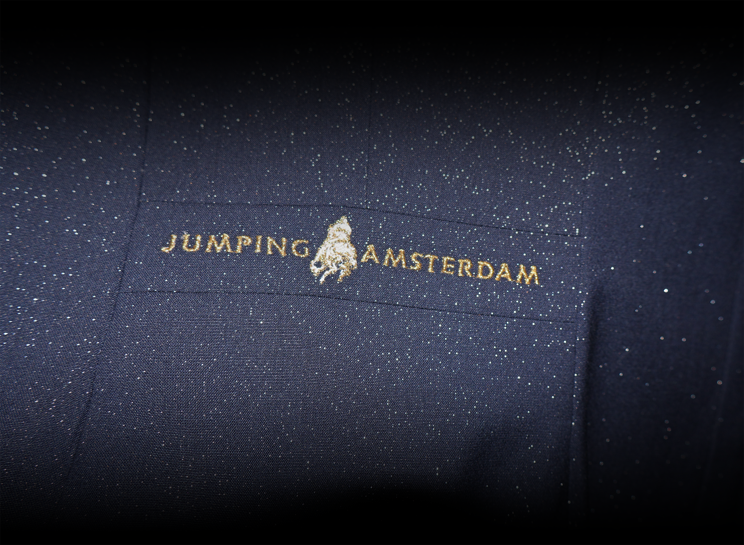 Detail of the back band of the JuulC x Jumping Amsterdam Show Coat 2026 version, embroidered with the Jumping Amsterdam logo
