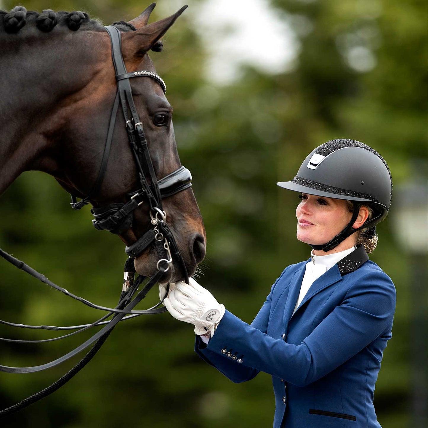 Model touching her horse's nose wearing the JuulC Royal Blue Show Coat for women with black accents and details